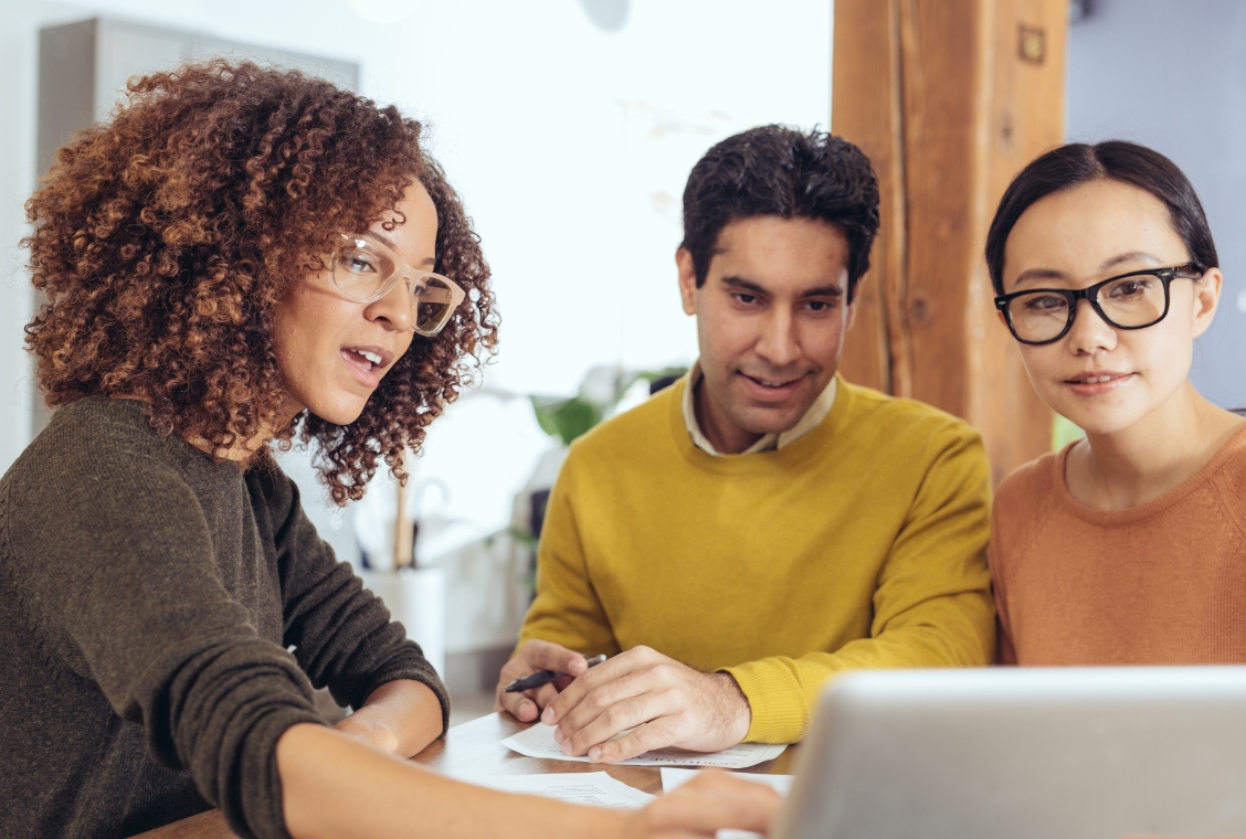 Couple sitting at a table with an advisor who is explaining something on her computer.