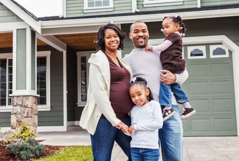 Family standing outside of house smiling.